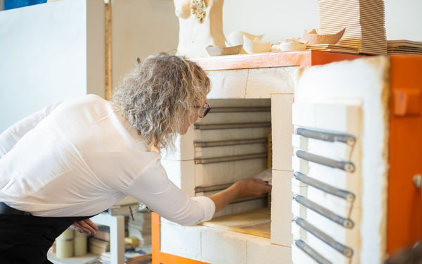 Potter loading a piece into an electric kiln in a bright studio